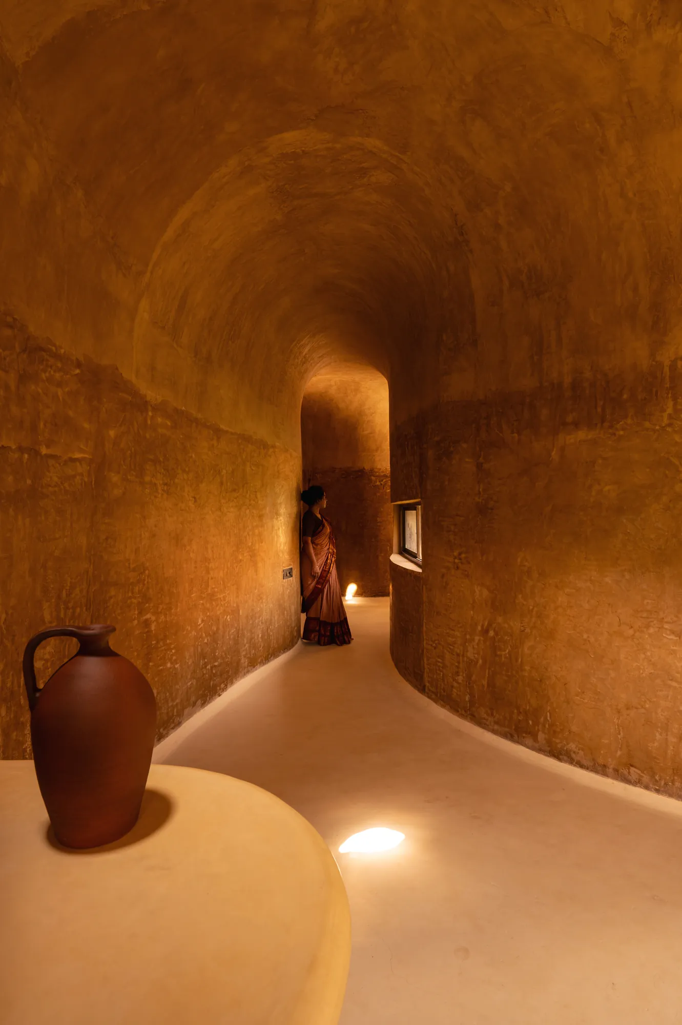 A corridor folding like a cave, finished in mud plaster